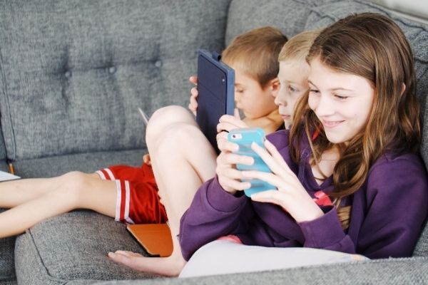 kids seating on couch and playing on mobile phone